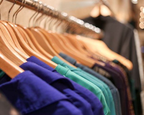 Several cool colored shirts hang on wooden hangers across a rack.